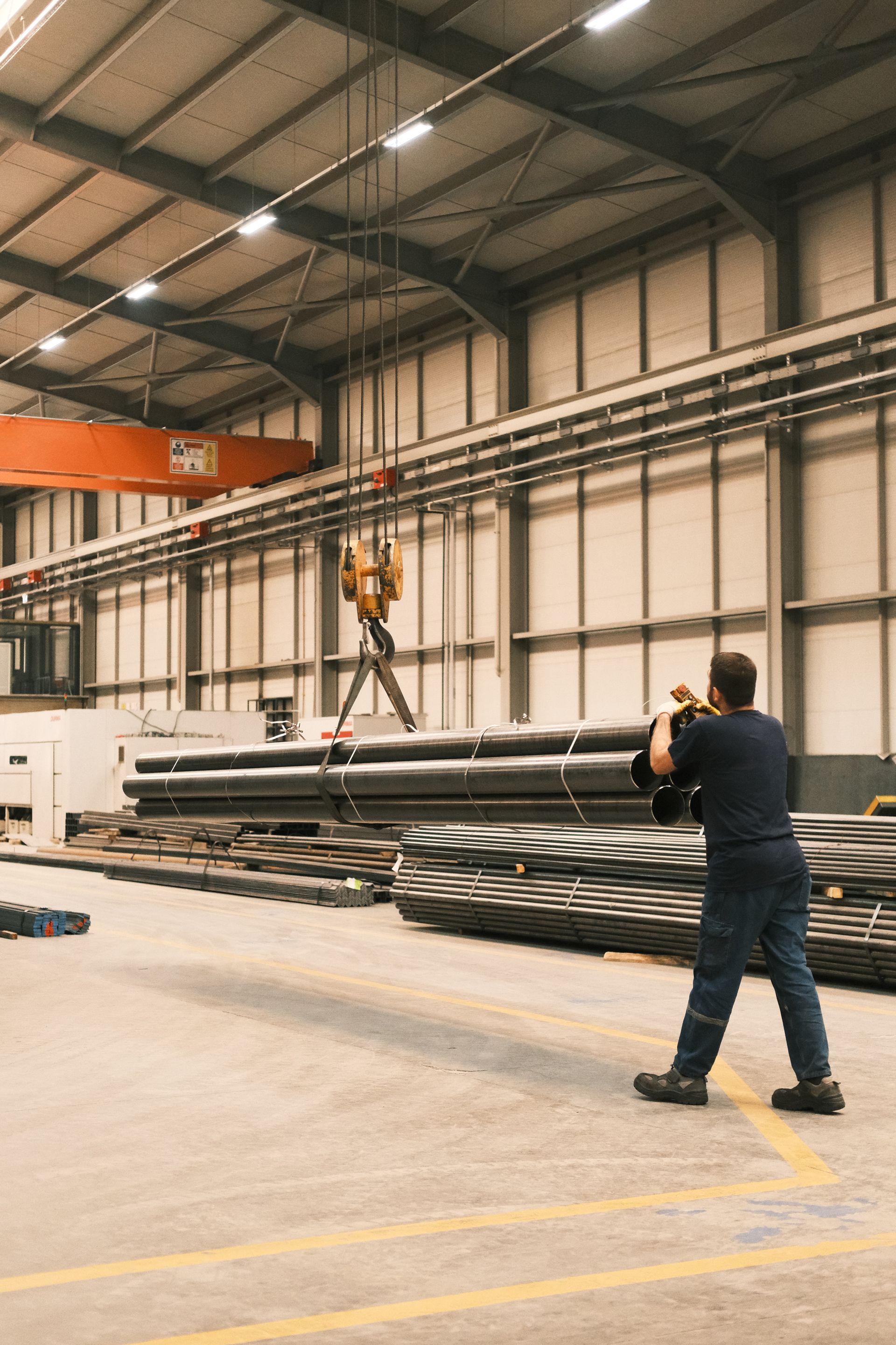 Manufacturing floor worker guiding an overhead crane with steel pipe